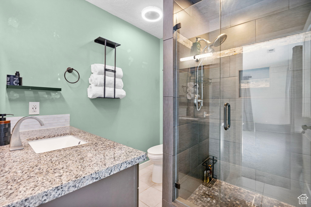Bathroom with toilet, a shower stall, vanity, and tile patterned flooring