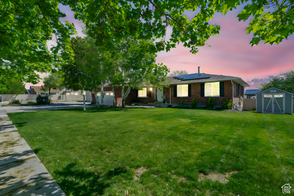 Single story home featuring fence, brick siding, a storage unit, solar panels, and a front lawn