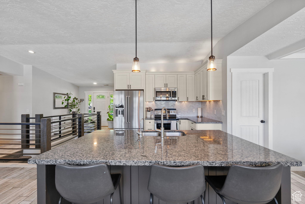 Kitchen with a sink, a kitchen breakfast bar, white cabinetry, and appliances with stainless steel finishes