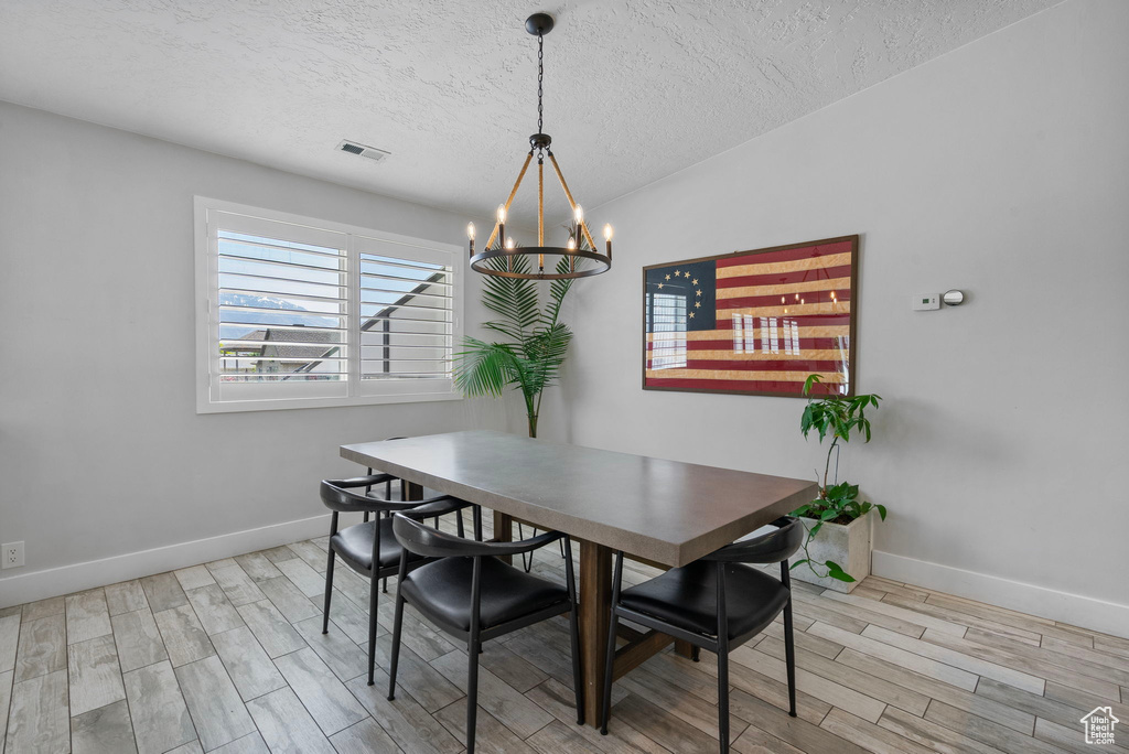 Dining area featuring an inviting chandelier, wood finished floors, a textured ceiling, visible vents, and baseboards