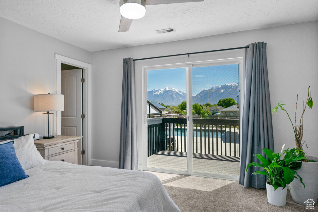 Carpeted bedroom featuring a ceiling fan, a mountain view, a textured ceiling, visible vents, and access to outside