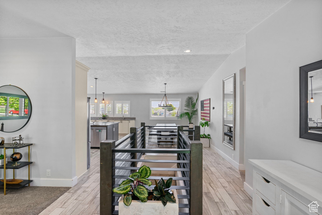 Corridor with a textured ceiling, baseboards, and light wood-type flooring