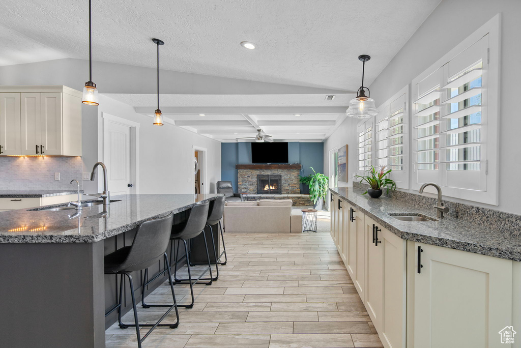 Kitchen with backsplash, a stone fireplace, light wood-type flooring, and a sink
