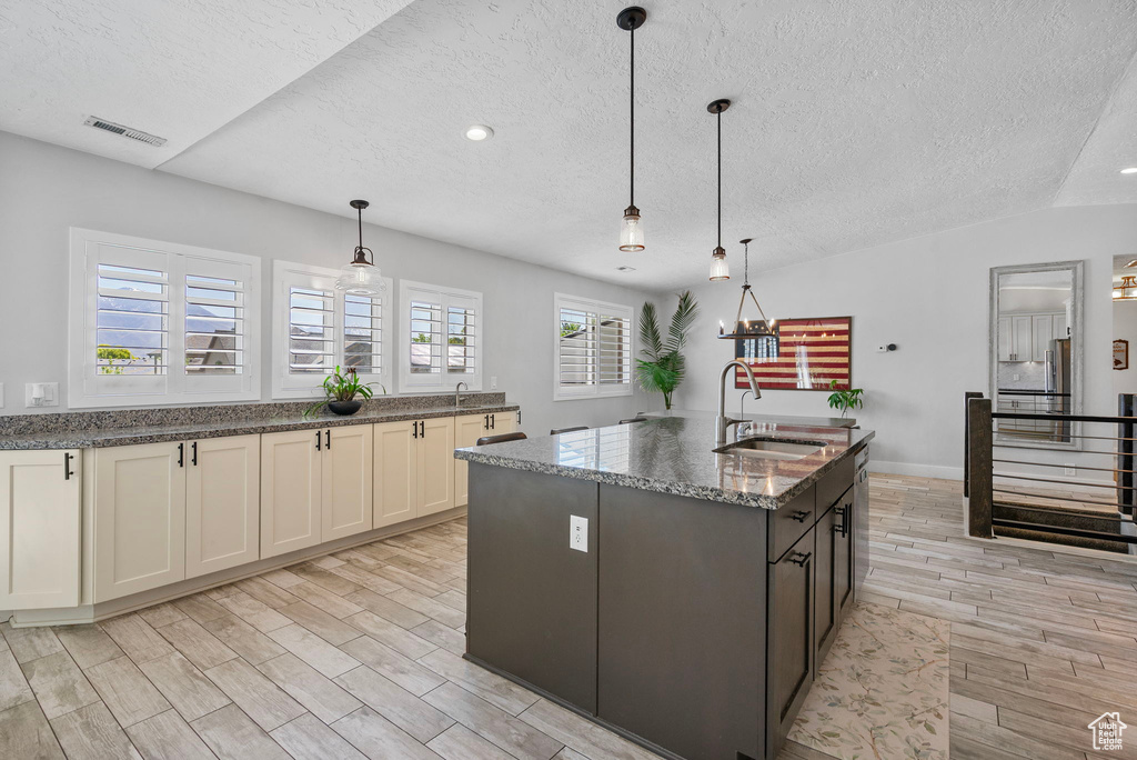 Kitchen with a sink, dark stone counters, a textured ceiling, visible vents, and wood tiled floor