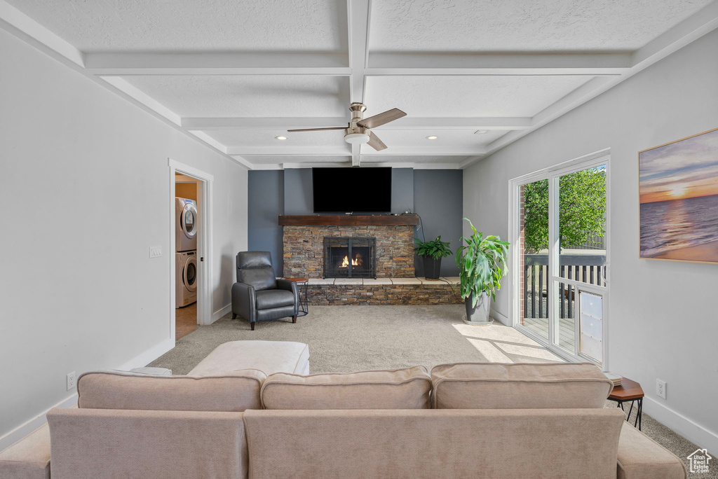 Living area with a fireplace, ceiling fan, carpet floors, stacked washing maching and dryer, and baseboards