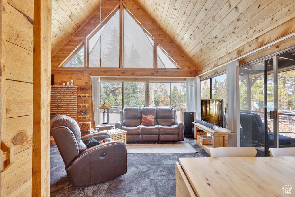Living room with high vaulted ceiling, wood ceiling, dark colored carpet, and wooden walls