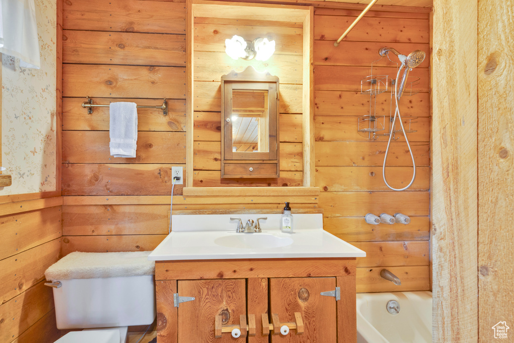 Bathroom with toilet, vanity, wood walls, and shower / tub combo