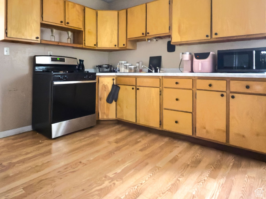 Kitchen with light wood-style floors, stainless steel gas stove, open shelves, and light countertops