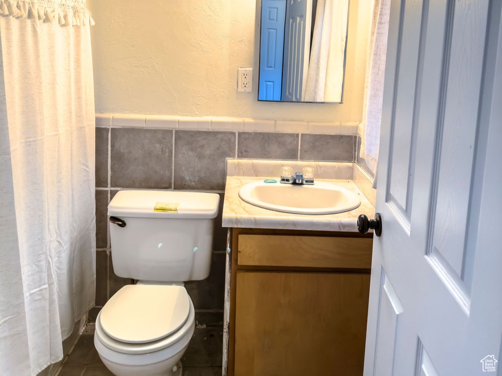 Full bath with tile walls, toilet, a wainscoted wall, vanity, and a textured ceiling