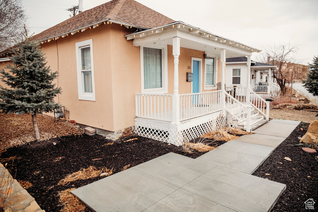 View of front of home featuring a porch, a shingled roof, and stucco siding
