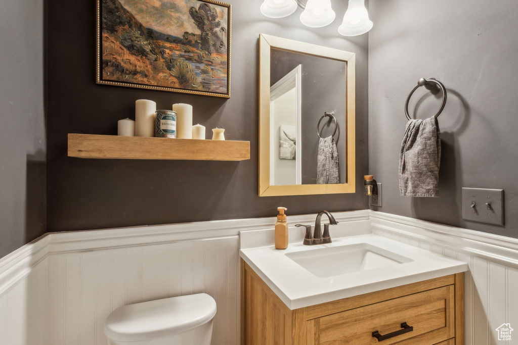 Bathroom featuring vanity, a decorative wall, toilet, and wainscoting