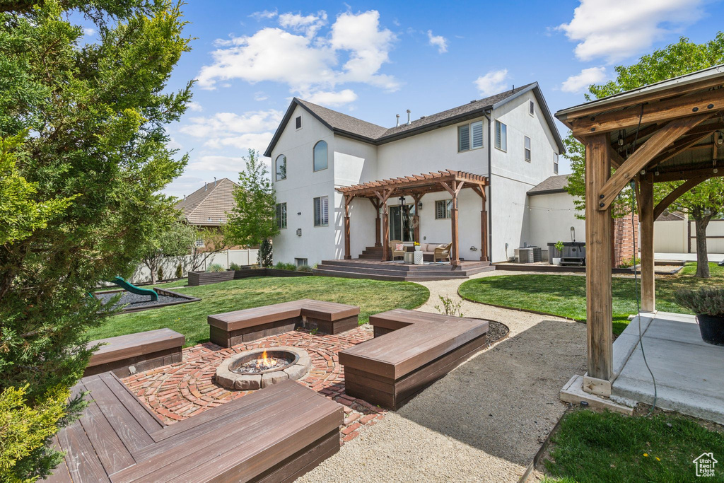 Rear view of house featuring an outdoor fire pit, stucco siding, a pergola, a lawn, and a patio area