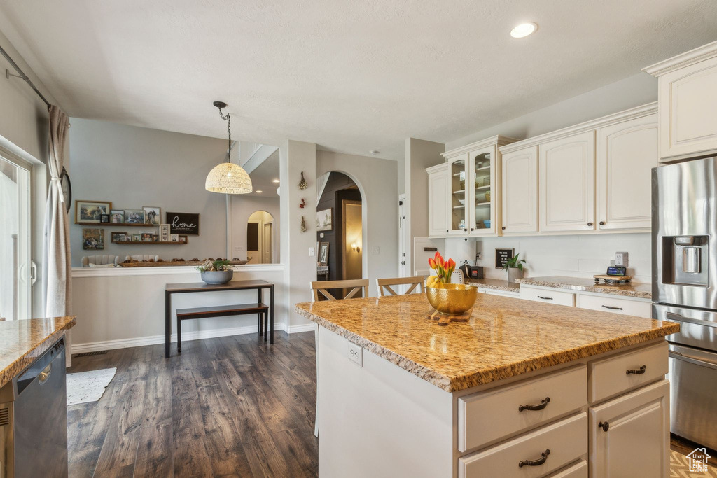 Kitchen with glass insert cabinets, stainless steel fridge with ice dispenser, dark wood-type flooring, arched walkways, and light stone counters