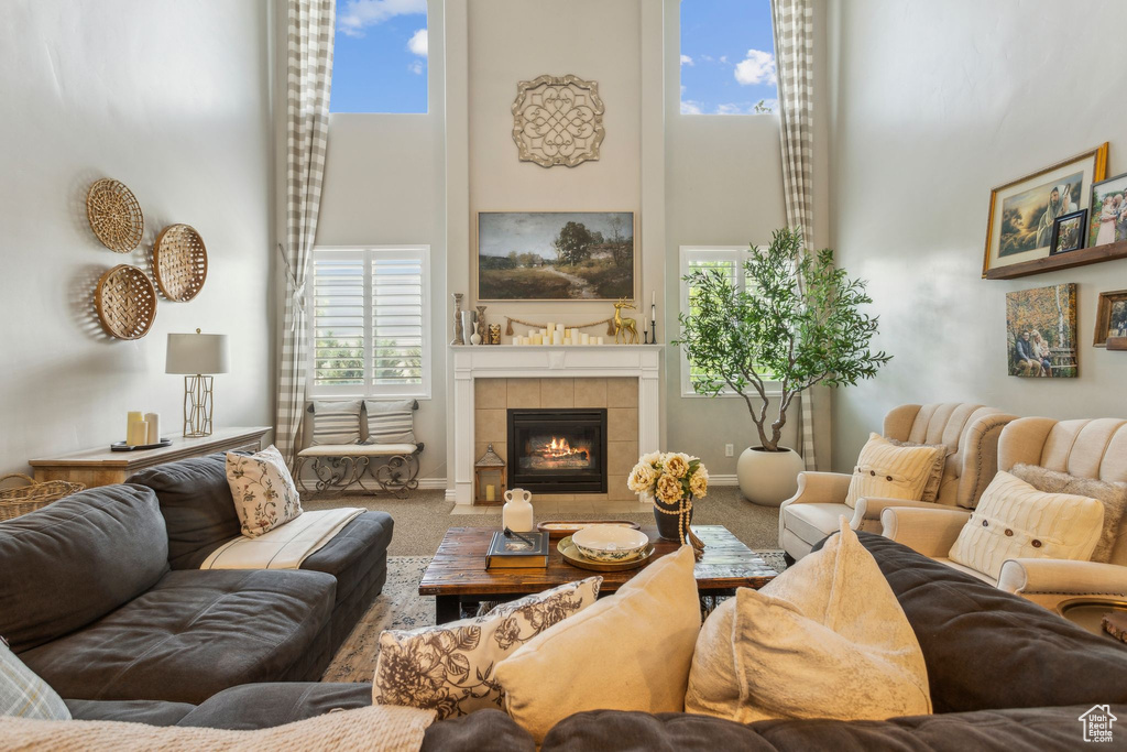Carpeted living room with a tiled fireplace, baseboards, and a towering ceiling