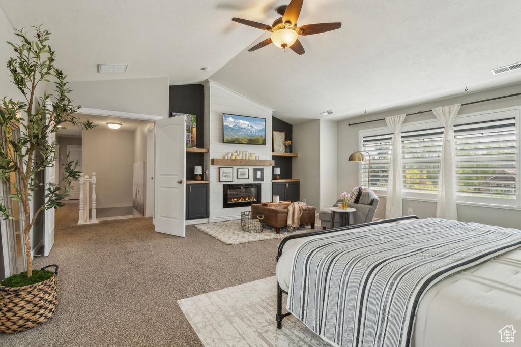Bedroom featuring vaulted ceiling, visible vents, a glass covered fireplace, and carpet floors