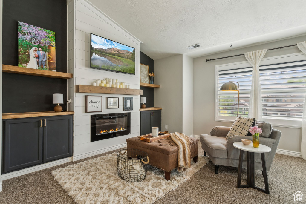 Carpeted living room with a large fireplace, a textured ceiling, lofted ceiling, and visible vents