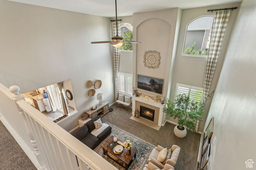 Living room featuring a towering ceiling, carpet, a fireplace, a ceiling fan, and baseboards