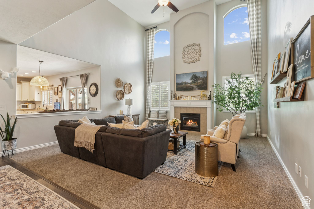 Carpeted living area featuring a tile fireplace, a ceiling fan, baseboards, and a towering ceiling