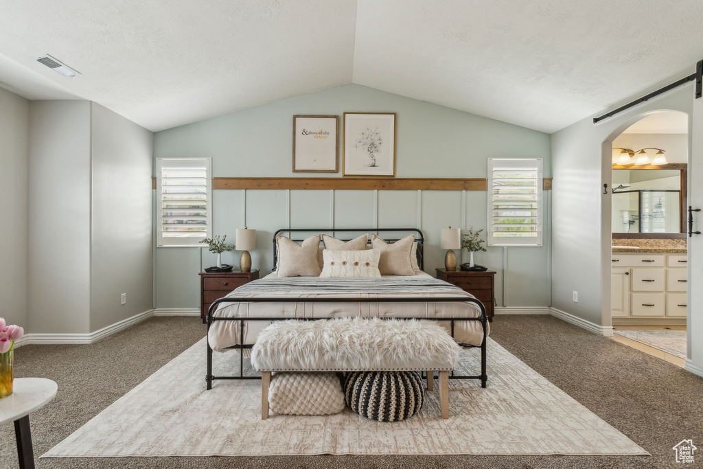 Bedroom with ensuite bath, visible vents, vaulted ceiling, carpet floors, and arched walkways
