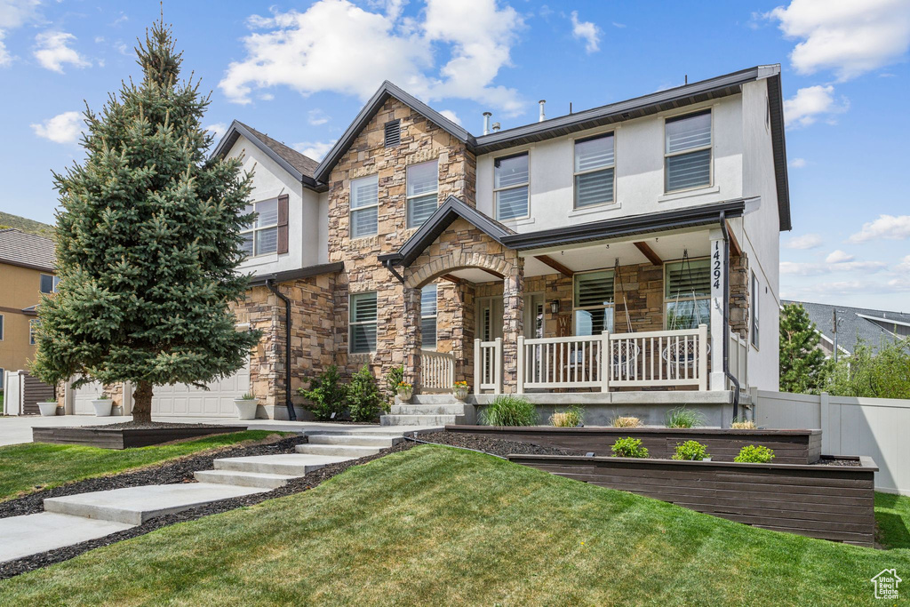 View of front of house featuring covered porch, fence, stone siding, stucco siding, and a front lawn