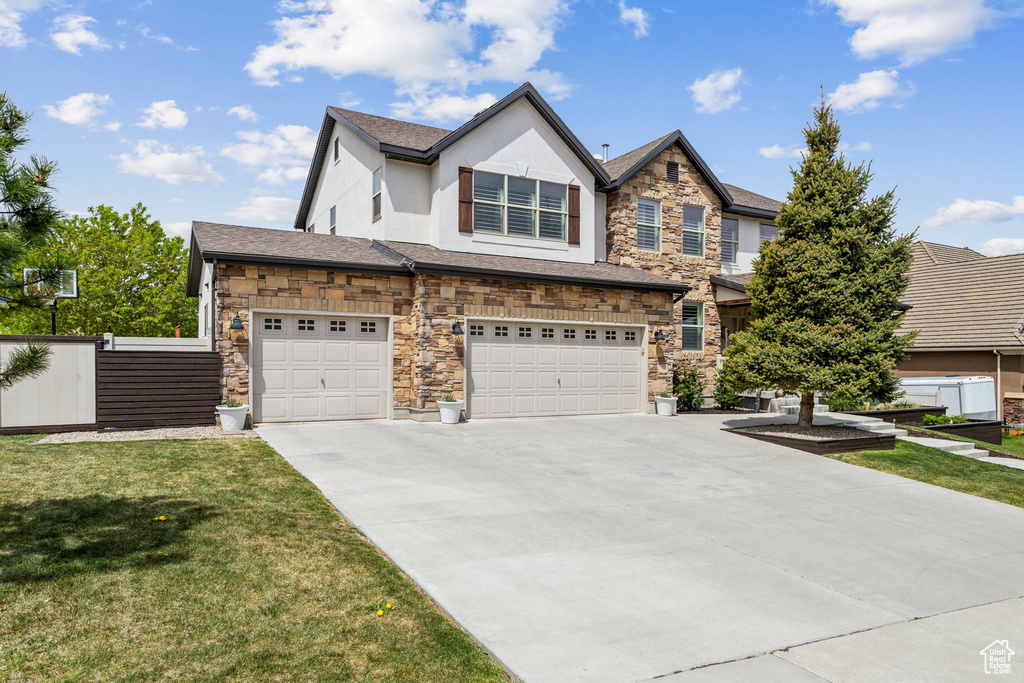 View of front facade featuring stone siding, concrete driveway, a garage, stucco siding, and a front lawn