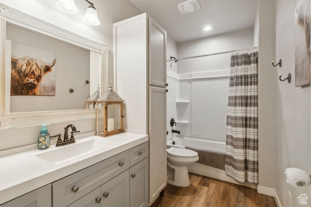 Bathroom with vanity, shower / bath combo, toilet, and wood finished floors