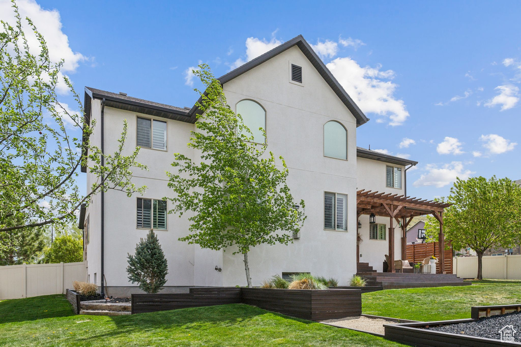 Rear view of house featuring a lawn, stucco siding, a pergola, a garden, and a fenced backyard