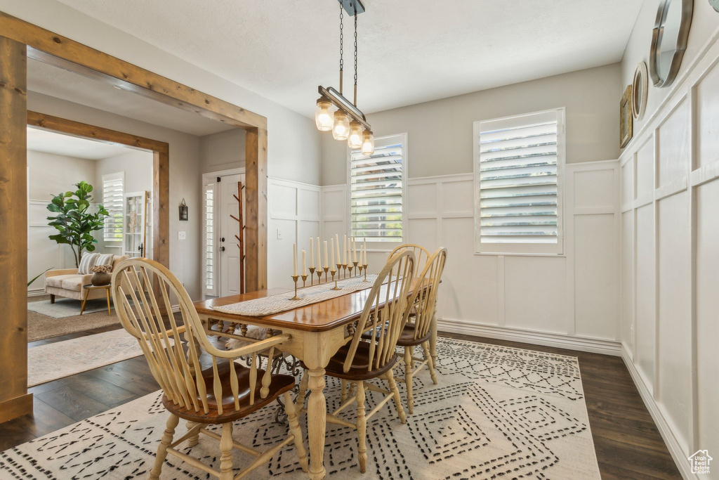 Dining space with dark wood-type flooring, a decorative wall, and wainscoting
