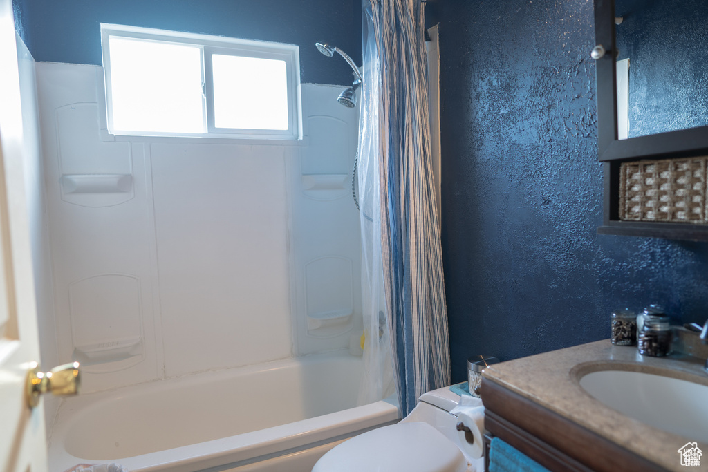 Full bath featuring vanity, toilet, a textured wall, and shower / tub combo