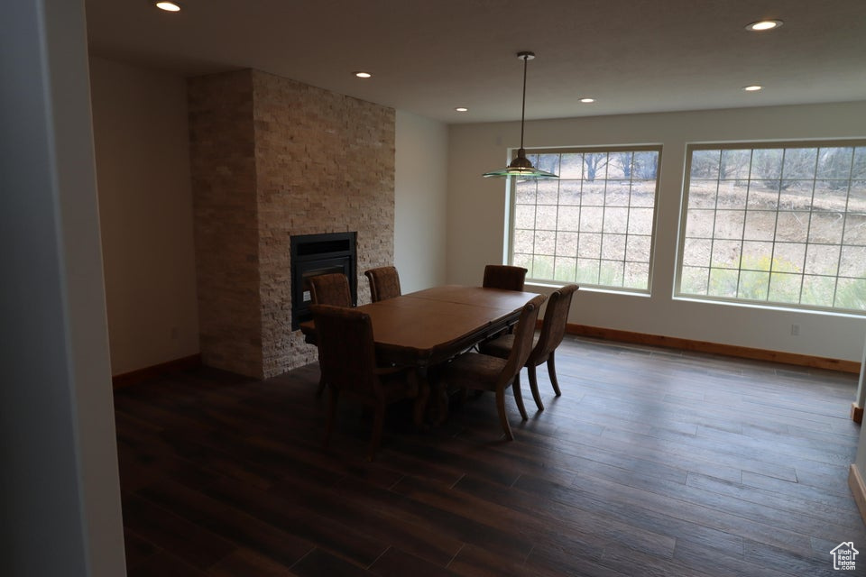 Dining area with baseboards, dark wood-style flooring, a stone fireplace, and recessed lighting