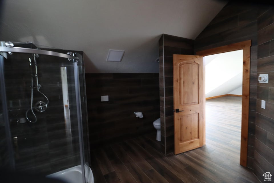 Bathroom featuring toilet, lofted ceiling, a shower stall, and wood finished floors