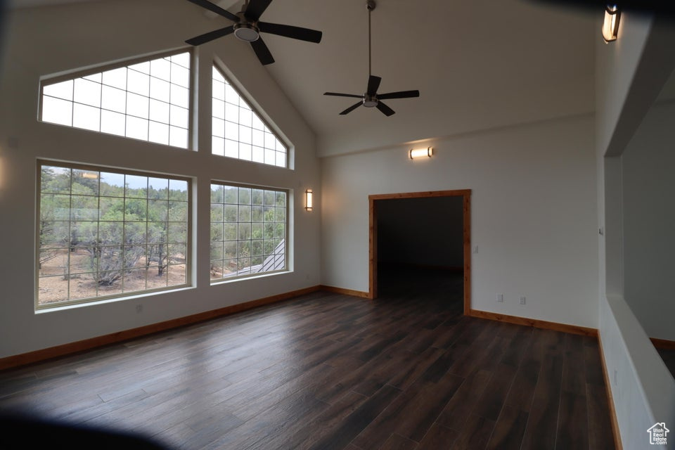 Unfurnished living room with baseboards, ceiling fan, high vaulted ceiling, and dark wood-type flooring