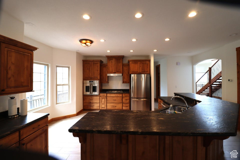 Kitchen with under cabinet range hood, dark countertops, appliances with stainless steel finishes, and a sink