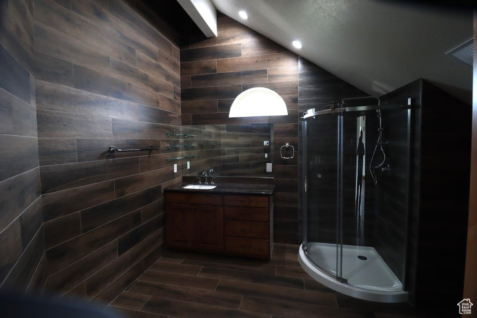Bathroom featuring a stall shower, tile walls, vaulted ceiling, vanity, and wood finished floors