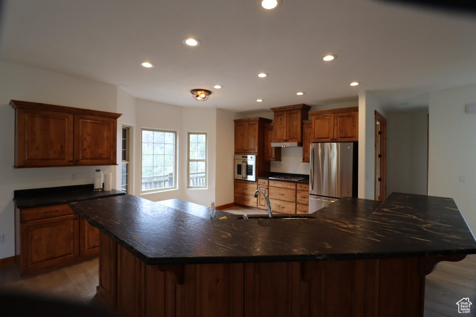 Kitchen with a sink, appliances with stainless steel finishes, a kitchen breakfast bar, recessed lighting, and light wood-style floors