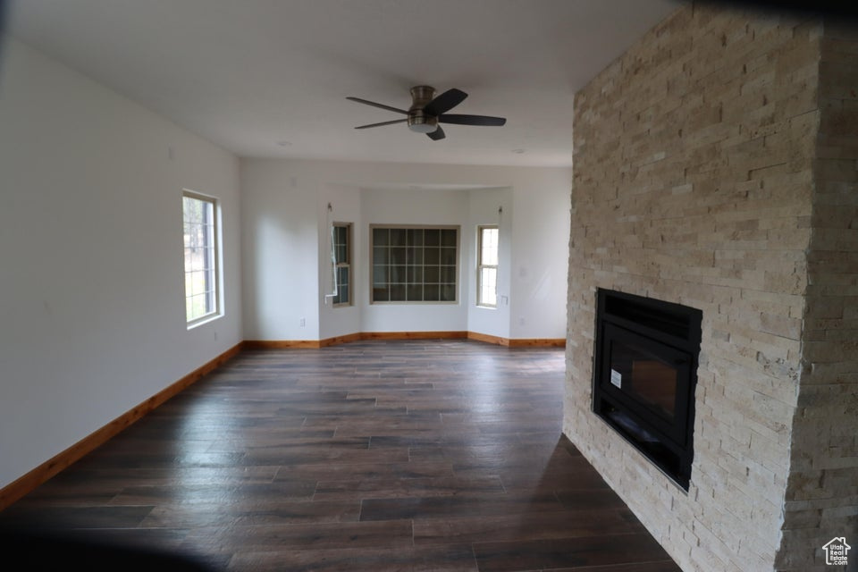 Unfurnished living room featuring a stone fireplace, baseboards, a ceiling fan, and wood finished floors