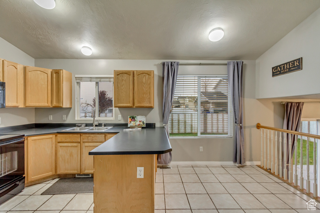 Kitchen with dark countertops, a sink, light tile patterned floors, black appliances, and light brown cabinets