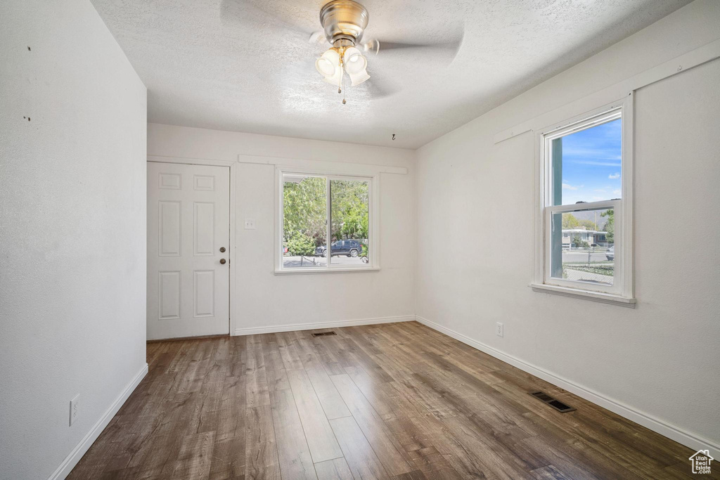 Spare room with wood finished floors, a textured ceiling, visible vents, baseboards, and ceiling fan