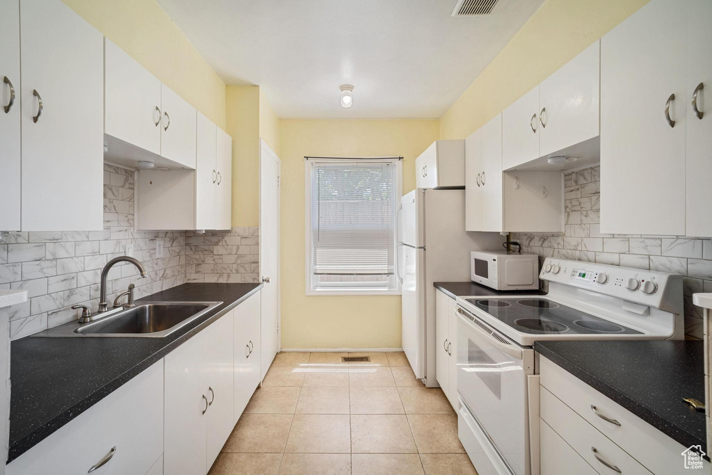 Kitchen featuring white appliances, a sink, decorative backsplash, dark countertops, and white cabinets