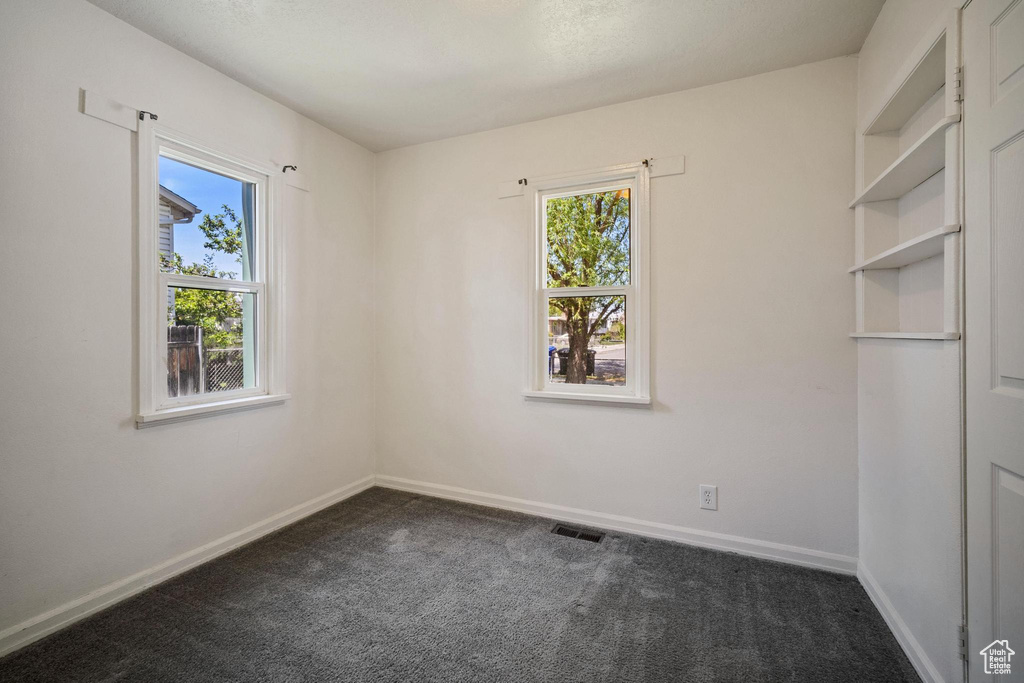 Empty room featuring dark colored carpet, baseboards, and visible vents