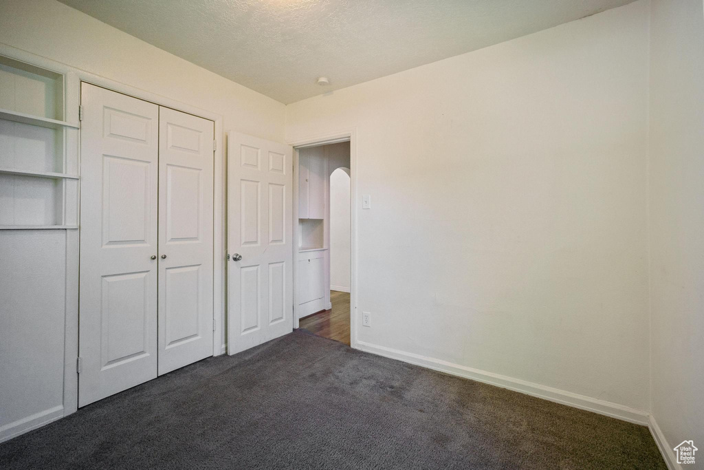 Unfurnished bedroom with a closet, baseboards, dark carpet, and arched walkways