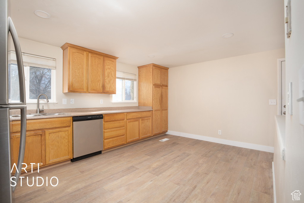 Kitchen with light wood finished floors, a sink, stainless steel appliances, baseboards, and light countertops