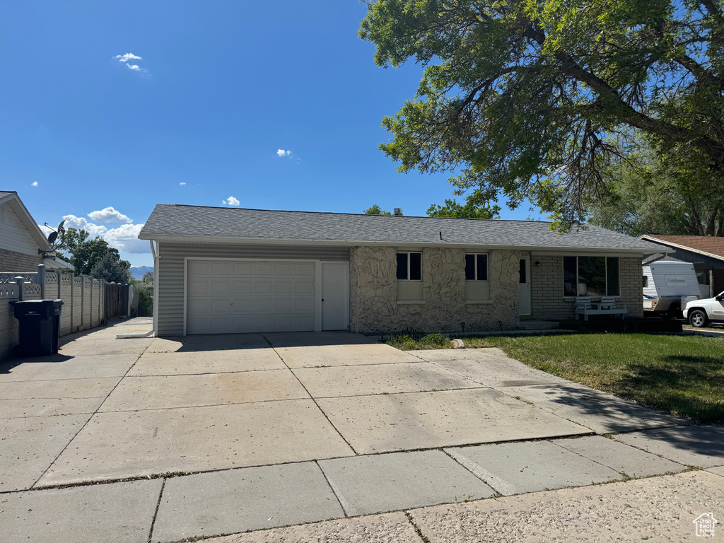 Ranch-style home featuring concrete driveway, an attached garage, fence, and stone siding
