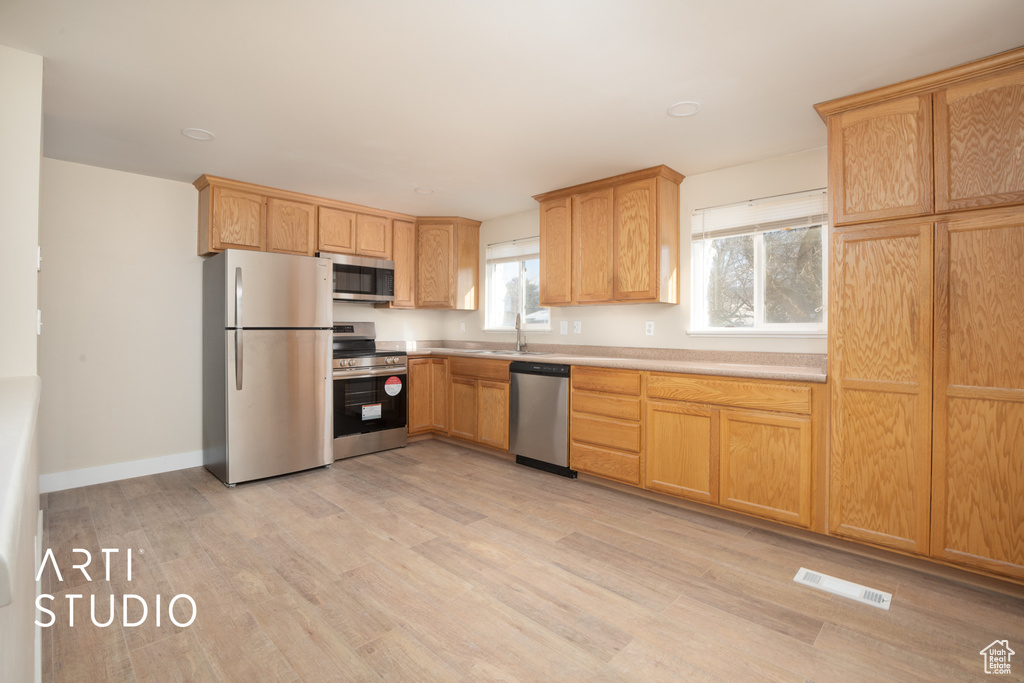 Kitchen with appliances with stainless steel finishes, visible vents, light countertops, baseboards, and light wood-style floors