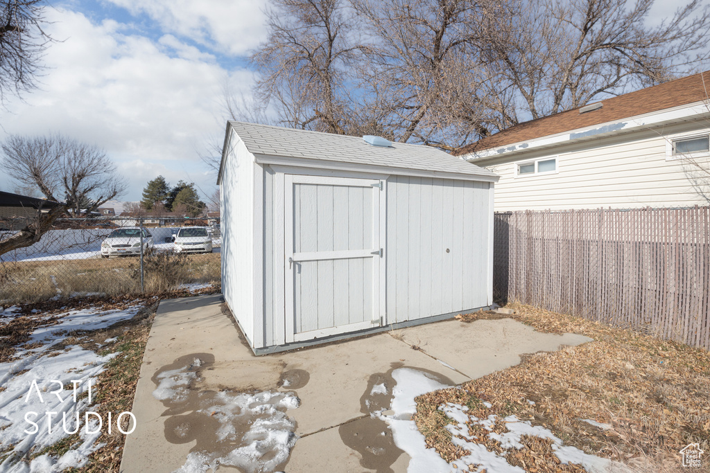 Snow covered structure featuring an outbuilding, a shed, and a fenced backyard