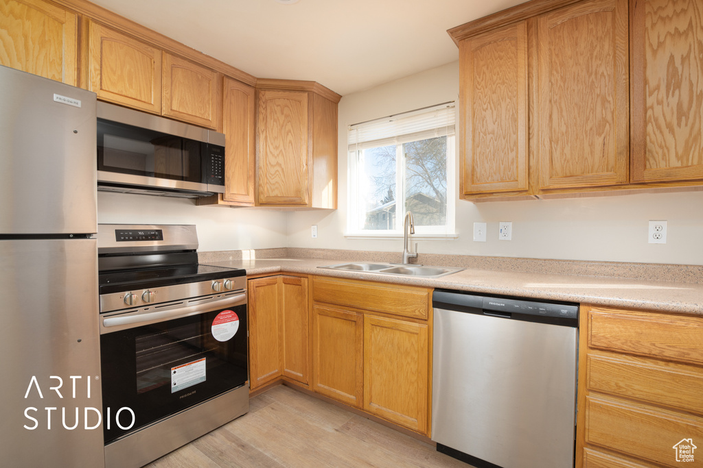 Kitchen with a sink, stainless steel appliances, light countertops, and light wood-style flooring