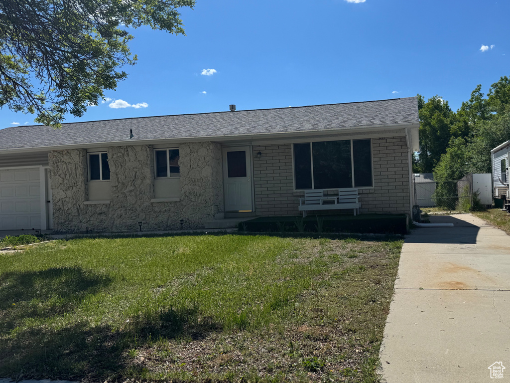 Ranch-style home featuring a front yard, concrete driveway, brick siding, stone siding, and a shingled roof