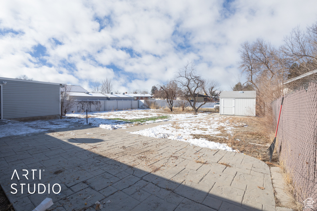 Yard layered in snow with a storage shed, an outbuilding, fence, and a patio