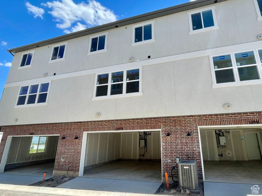 Rear view of house featuring cooling unit, stucco siding, brick siding, and an attached garage