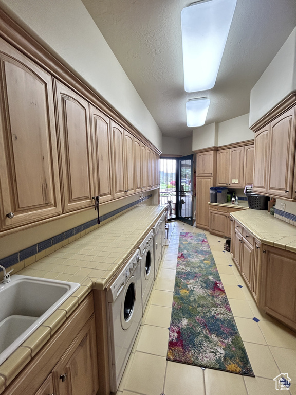 Laundry room with light tile patterned floors, laundry area, washing machine and dryer, and a sink